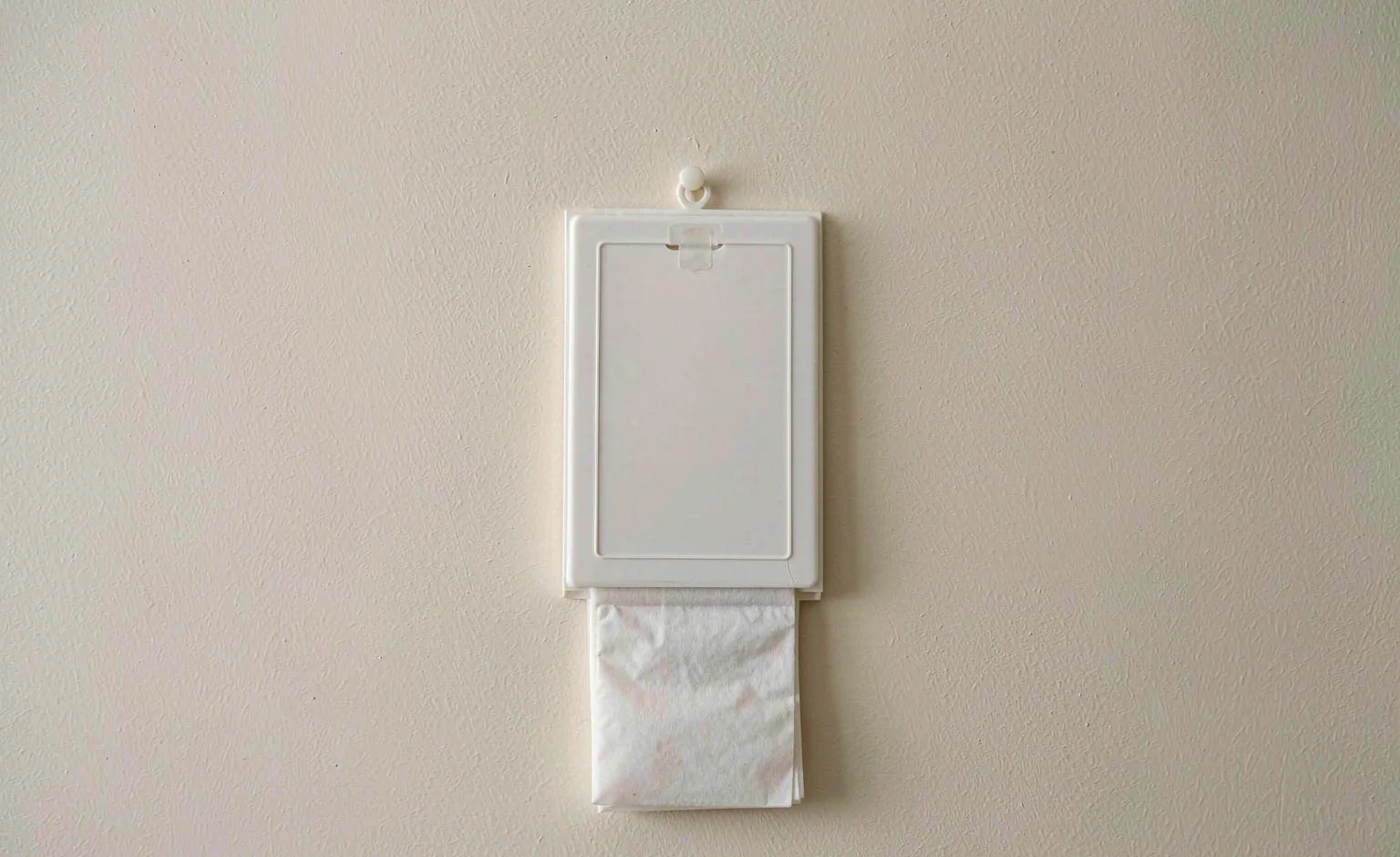 A simple wall-mounted film pack of white nonwoven sheets photographed flat against a plain wall.
