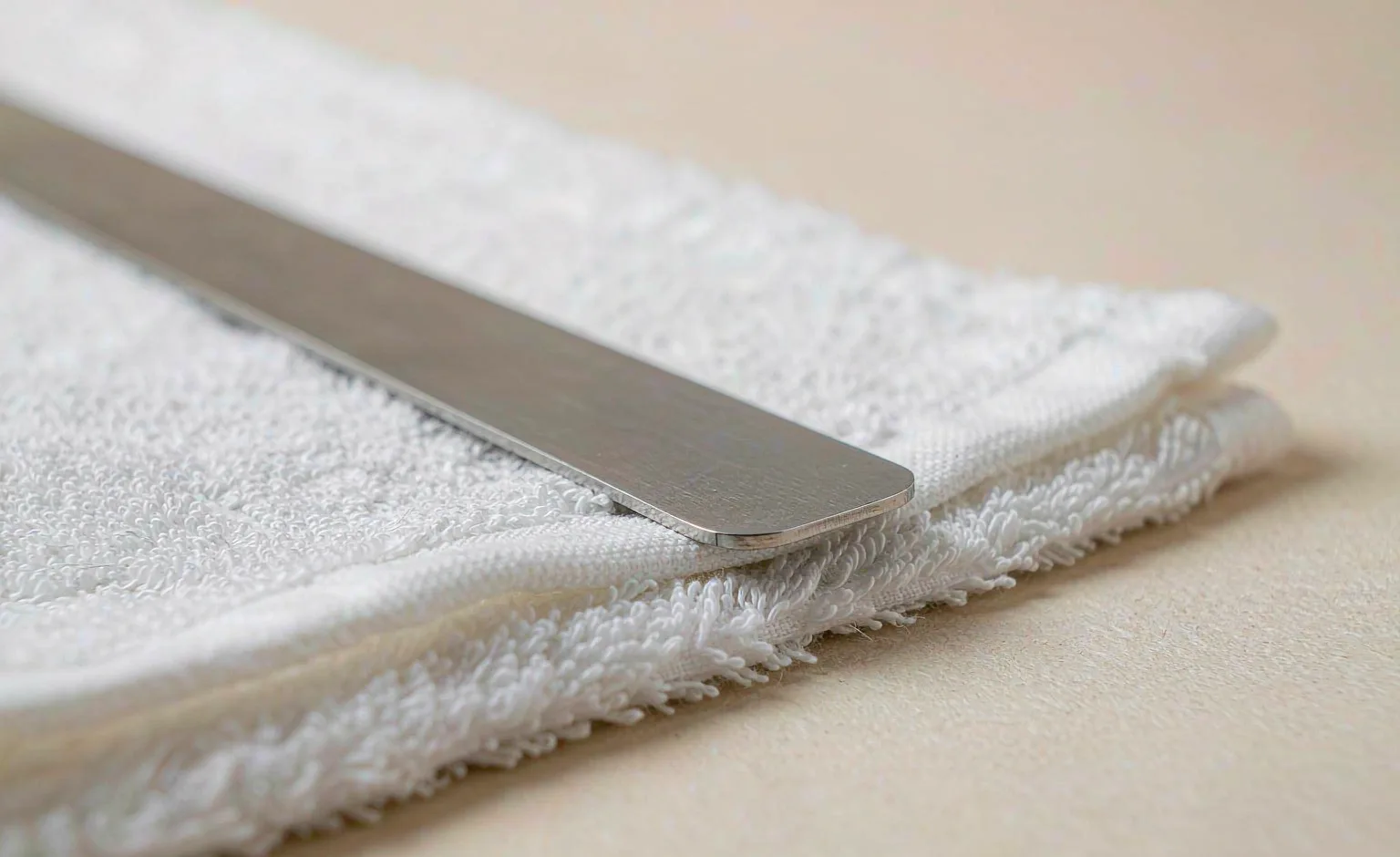 A steel ruler laid across a folded white nonwoven sheet on a warm paper surface.